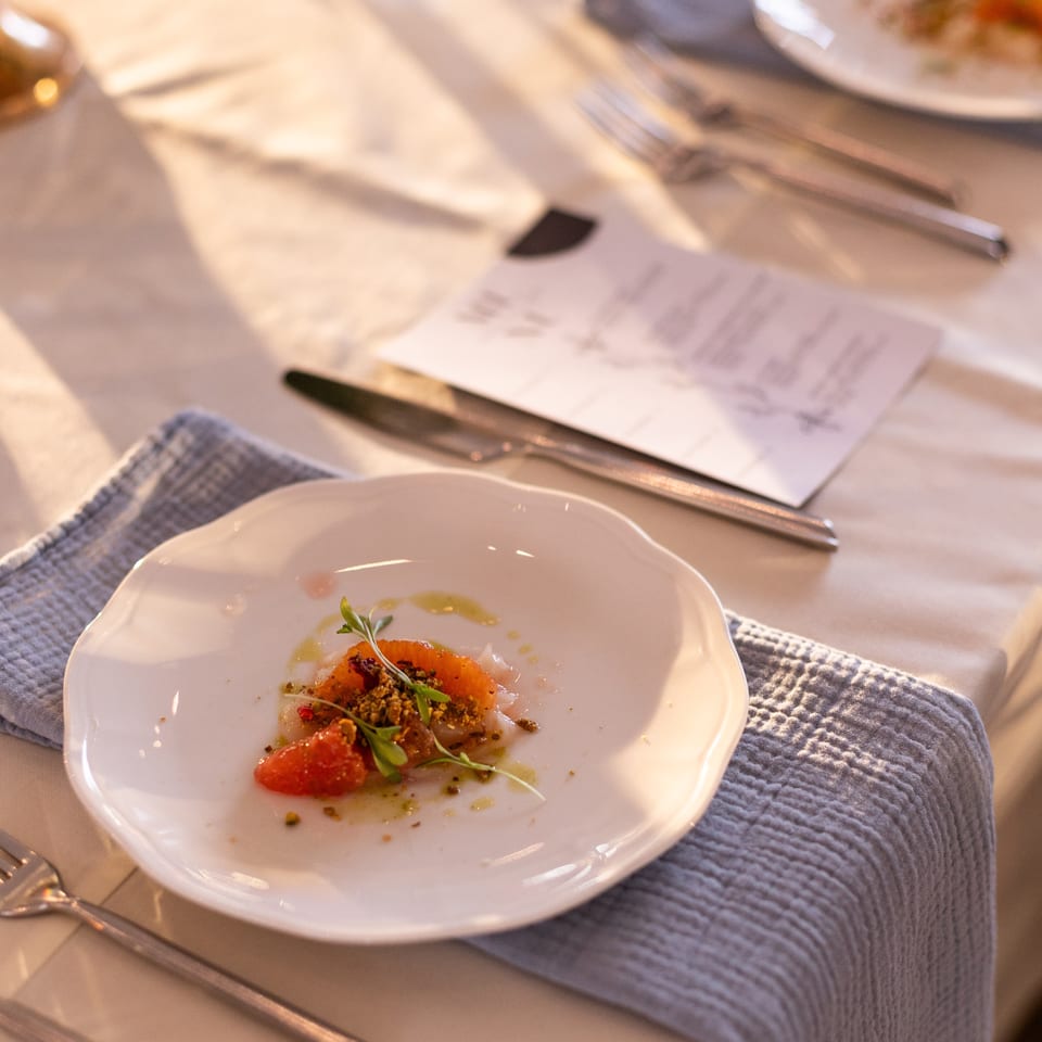 Elegant restaurant table setting with a plated gourmet dish garnished with microgreens, cutlery, folded napkins, and wine glasses.