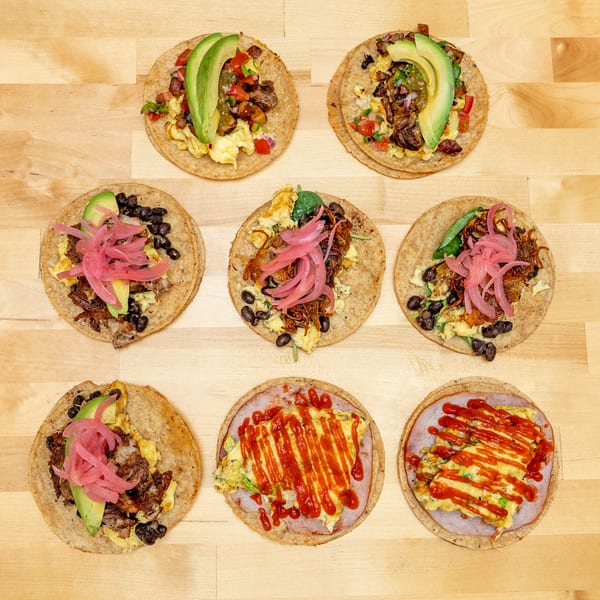 Overhead display of assorted breakfast tostadas topped with eggs, avocado, black beans, pickled onions, meats, and hot sauce.