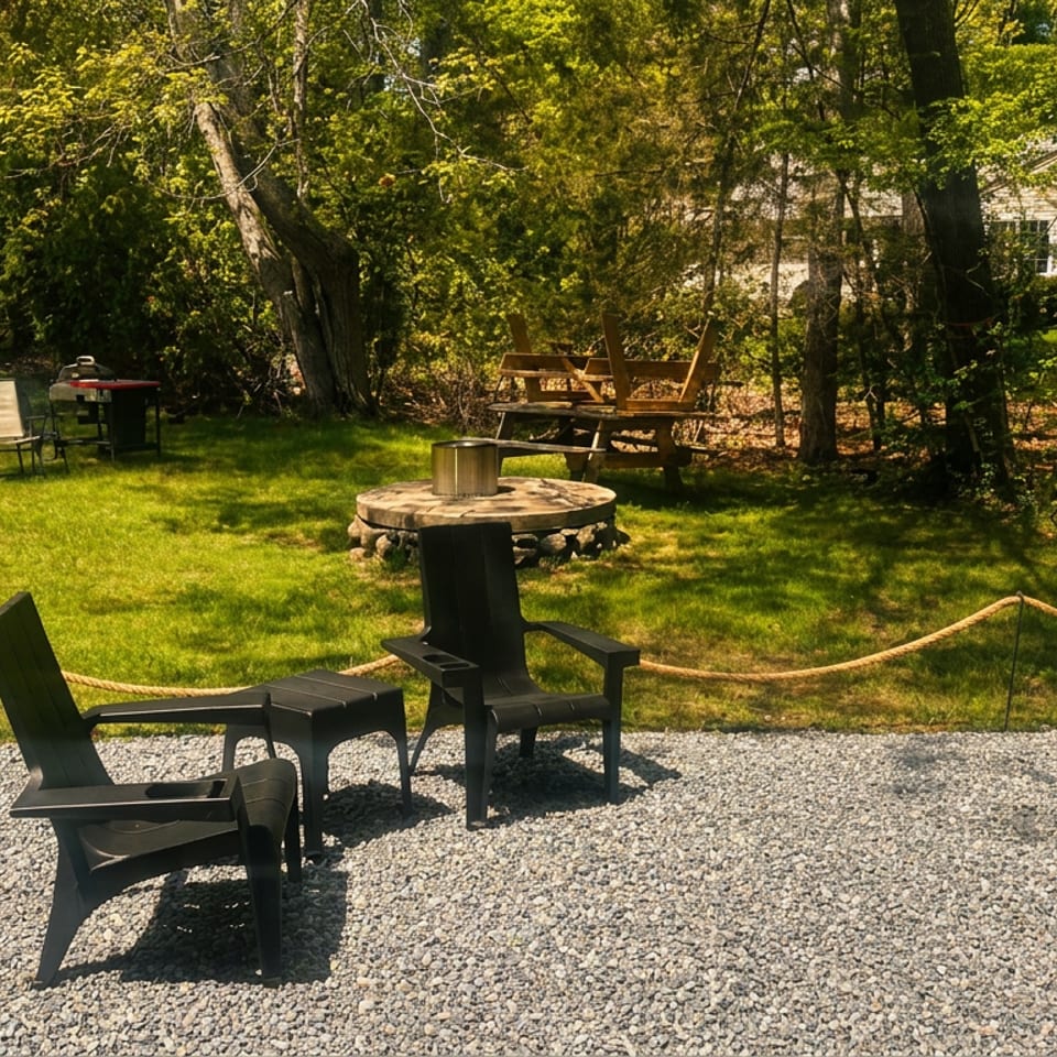 A woman holds takeout food on a gravel patio with outdoor chairs, fire pit, and lush greenery.