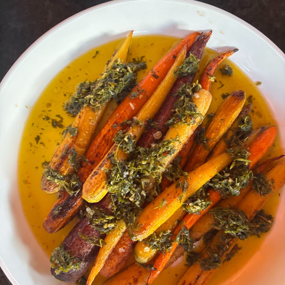 Roasted multicolored carrots drizzled with golden oil and topped with chopped herbs on a white plate.