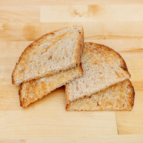 Several slices of toasted rustic bread arranged on a light wooden surface.