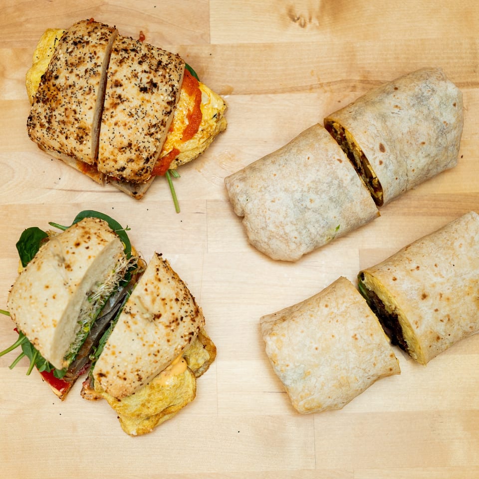 Assorted toasted sandwiches and sliced burritos arranged on a light wooden table.