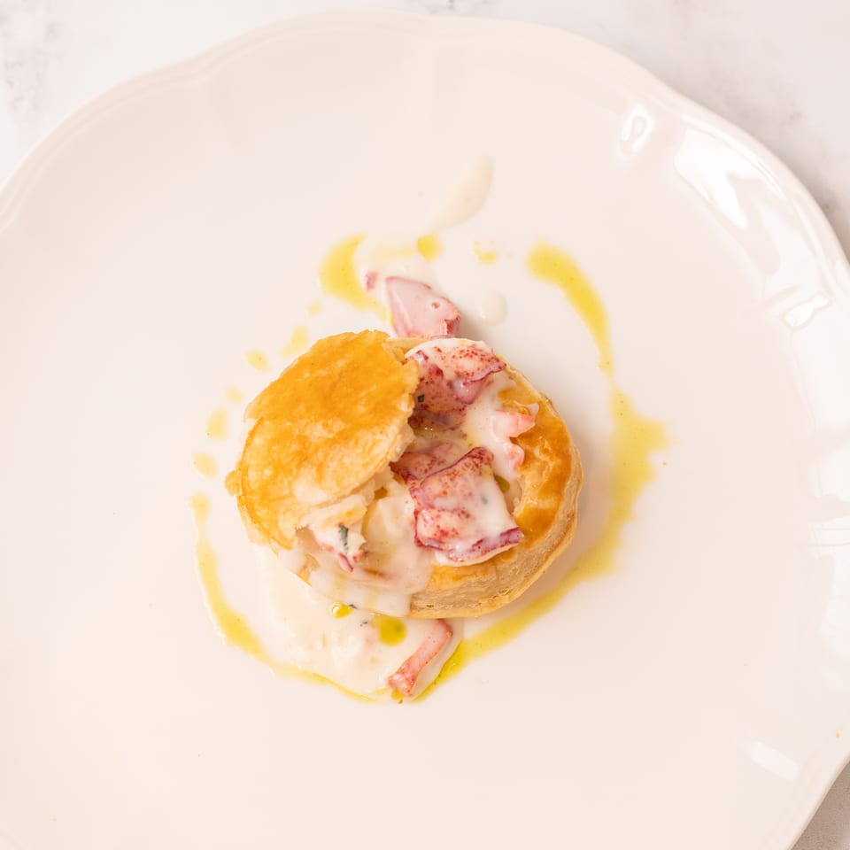 Golden pastry filled with lobster and creamy sauce, drizzled with olive oil on a white plate.