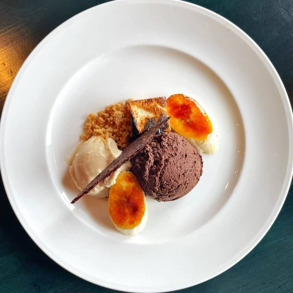 Dessert plate featuring chocolate mousse, vanilla ice cream, caramelized fruit, crumble, and a chocolate wafer.