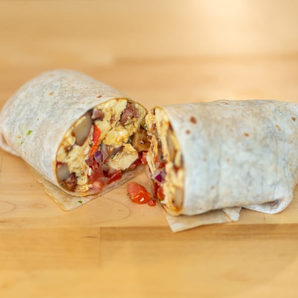 Two sliced chicken burritos filled with vegetables and sauce on a wooden table.