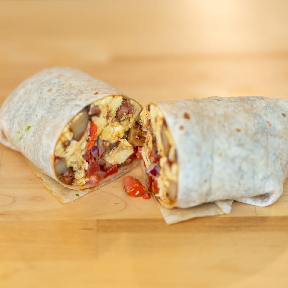 Two sliced chicken burritos filled with vegetables and sauce on a wooden table.